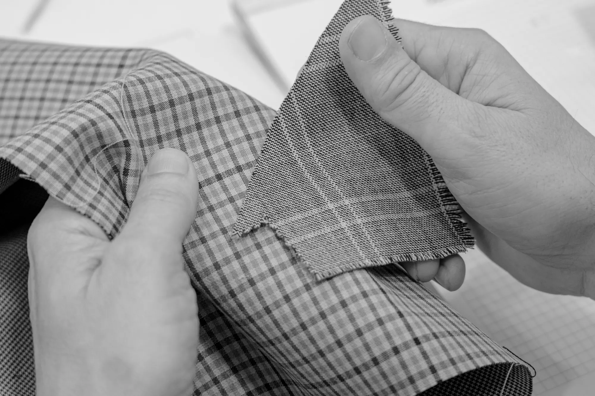 Hands comparing checked fabric samples for garment development